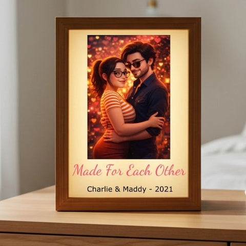 Wood framed light box glowing on a nightstand, showing an illustrated couple embracing above the words Made For Each Other and a sample name and year.