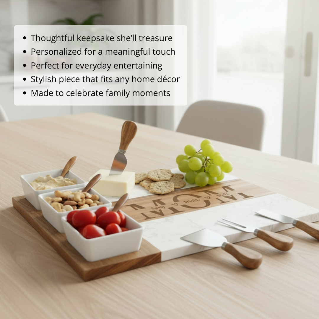 Personalized charcuterie board with marble and acacia wood, set with white bowls, spreaders, cheese knives, and sample engraved names on wooden inlay section, styled with cheese, grapes, crackers, and serving utensils.