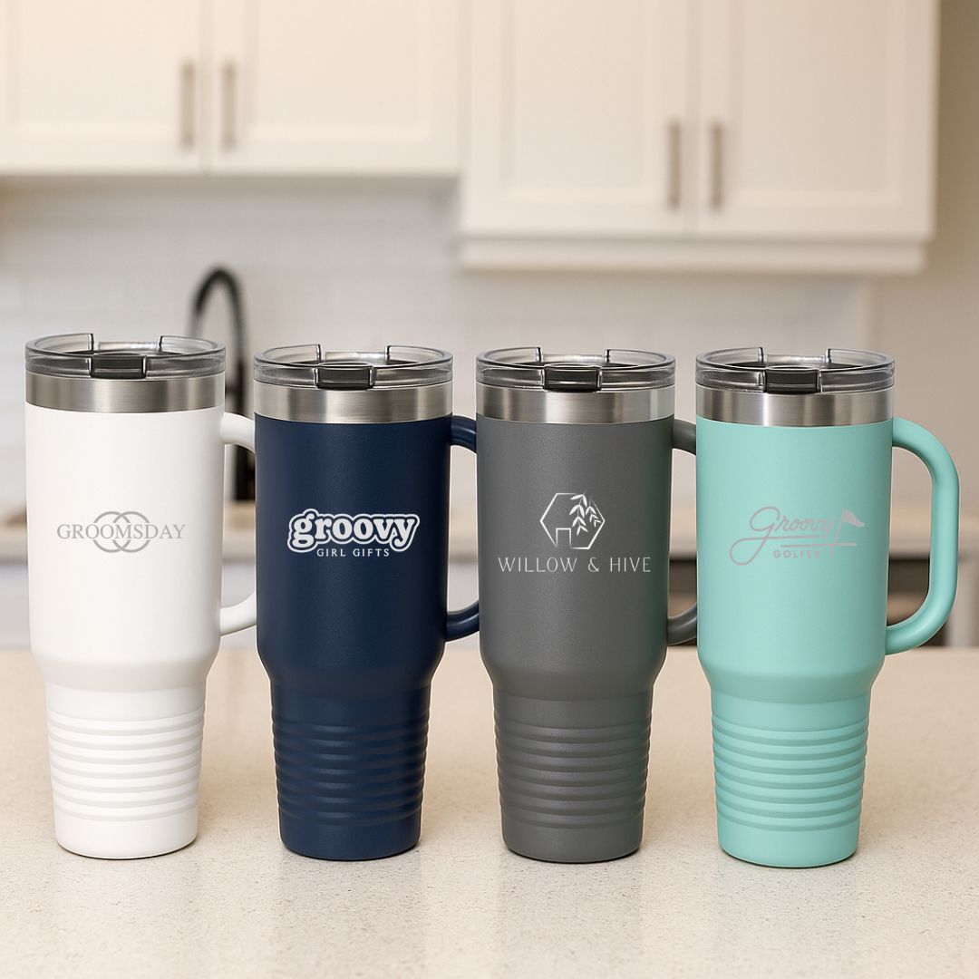 Four insulated 40 oz. tumblers in white, navy, gray, and mint with engraved logos including "GROOVY GIRL GIFTS," "WILLOW & HIVE," and other custom designs, displayed on a kitchen counter.