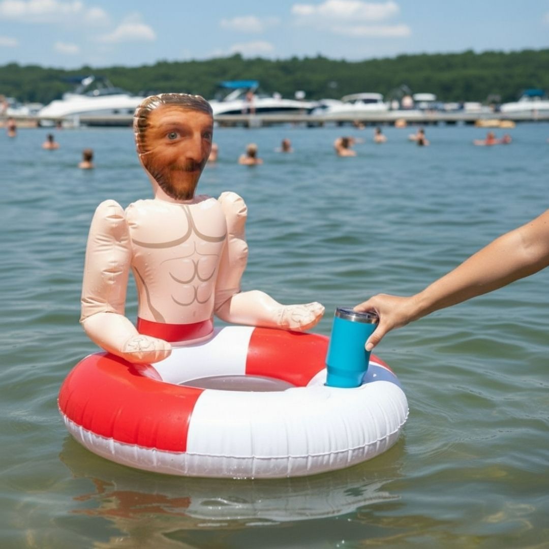Humorous pool float featuring an inflatable torso with a custom face photo, tan skin tone, and muscular chest design, floating in lake water with blue tumbler nearby