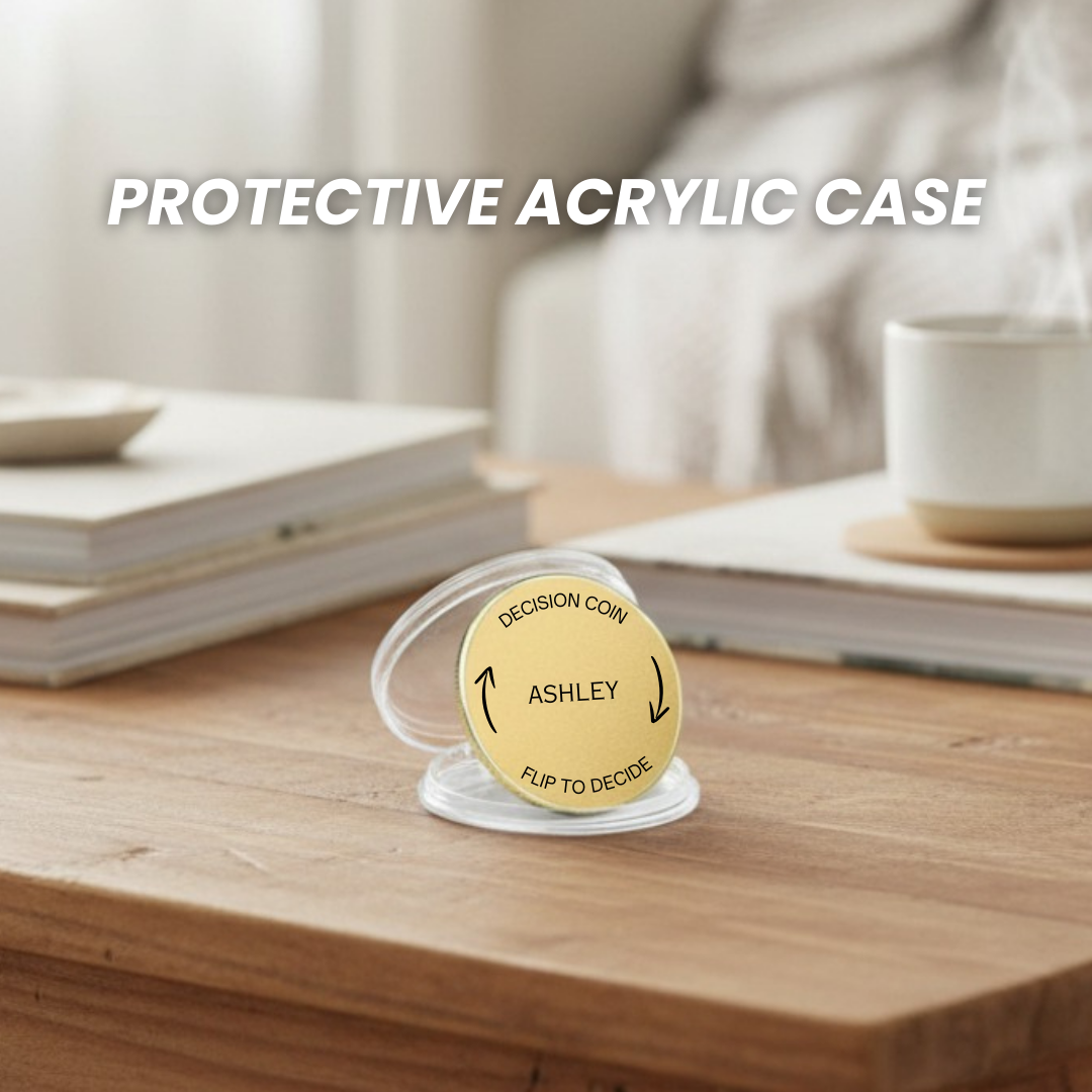 Gold brass decision coin engraved with sample name "ASHLEY" and "FLIP TO DECIDE" text, displayed in clear protective acrylic case on wooden surface