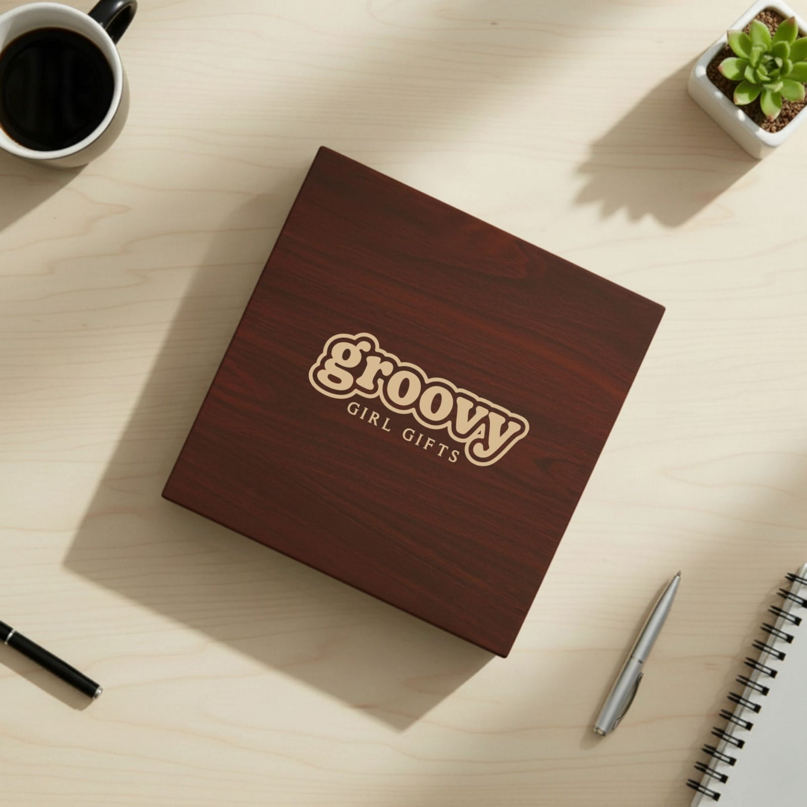 Dark cherry wood keepsake box with laser-engraved Groovy Girl Gifts logo on lid, displayed on light wood desk with coffee mug and succulent plant.