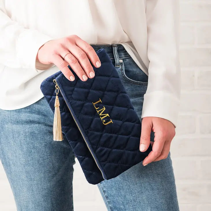 Navy quilted velvet clutch with gold tassel and zipper, held in hands, showing sample initials "LMU" embroidered on front