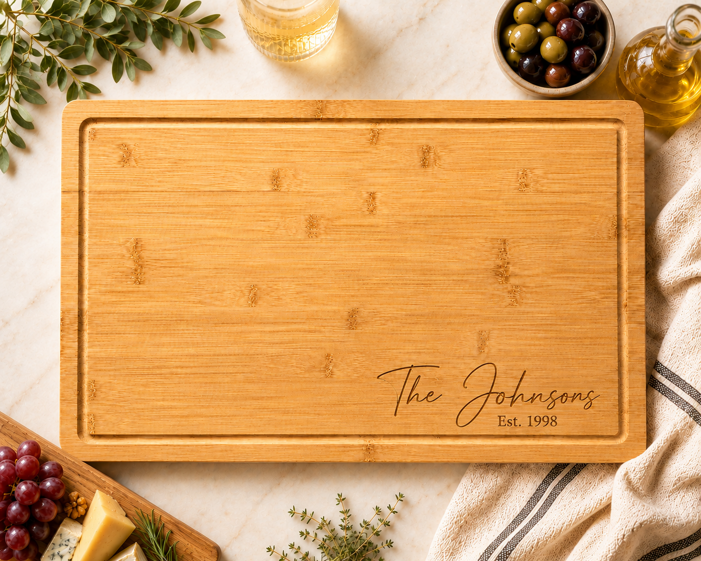 A rectangular bamboo cutting board with rounded corners, engraved with the name 'The Johnsons Est. 1998' in the bottom right corner.