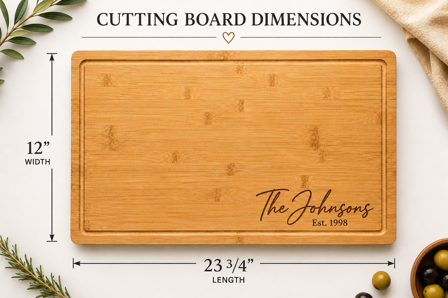A bamboo cutting board with engraved script text reading 'The Johnsons Est. 1998' shown on a white background with dimension labels indicating 12 inches wide by 23 3/4 inches long.