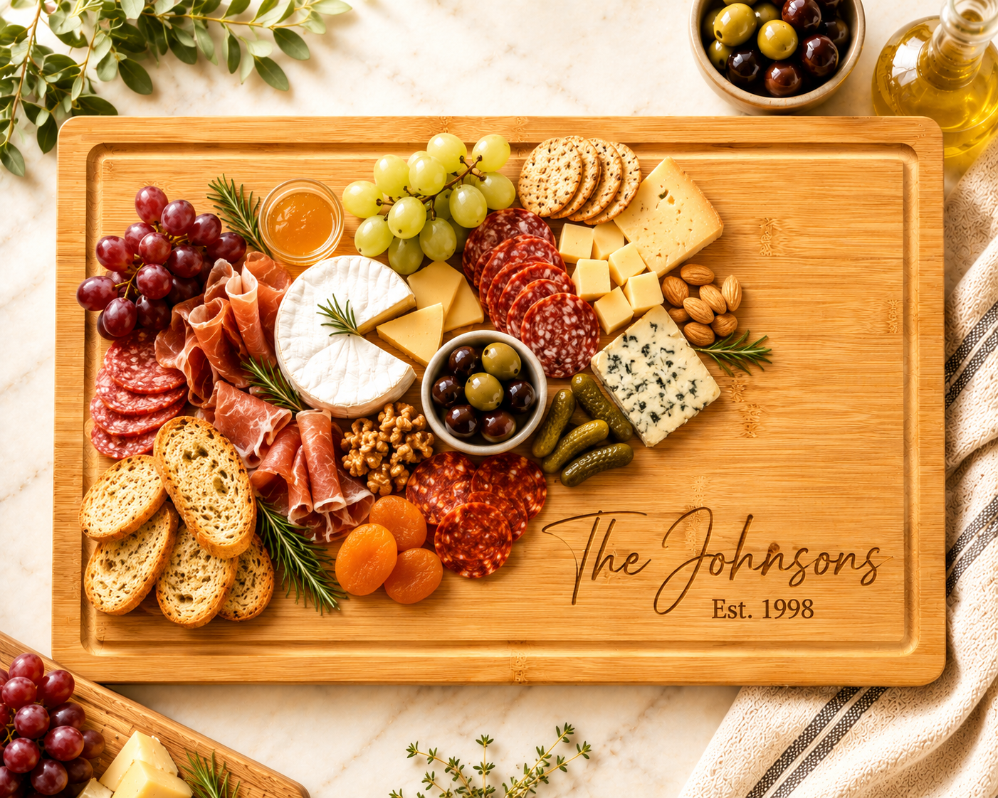 A large rectangular wooden charcuterie board engraved with 'The Johnsons Est. 1998' is filled with cheeses, cured meats, grapes, olives, crackers, bread, nuts, pickles, and apricots on a marble surface.
