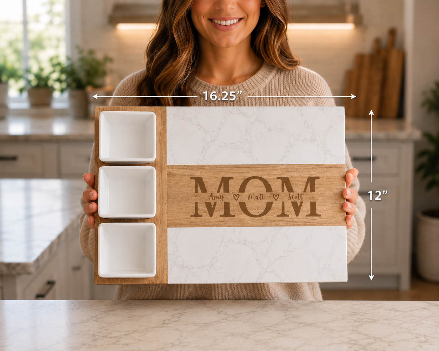 A woman in a beige sweater holds a rectangular wooden serving tray with three white square bowls on the left and a central wood panel engraved with 'MOM' and decorative text. White marble-patterned panels flank the center panel.