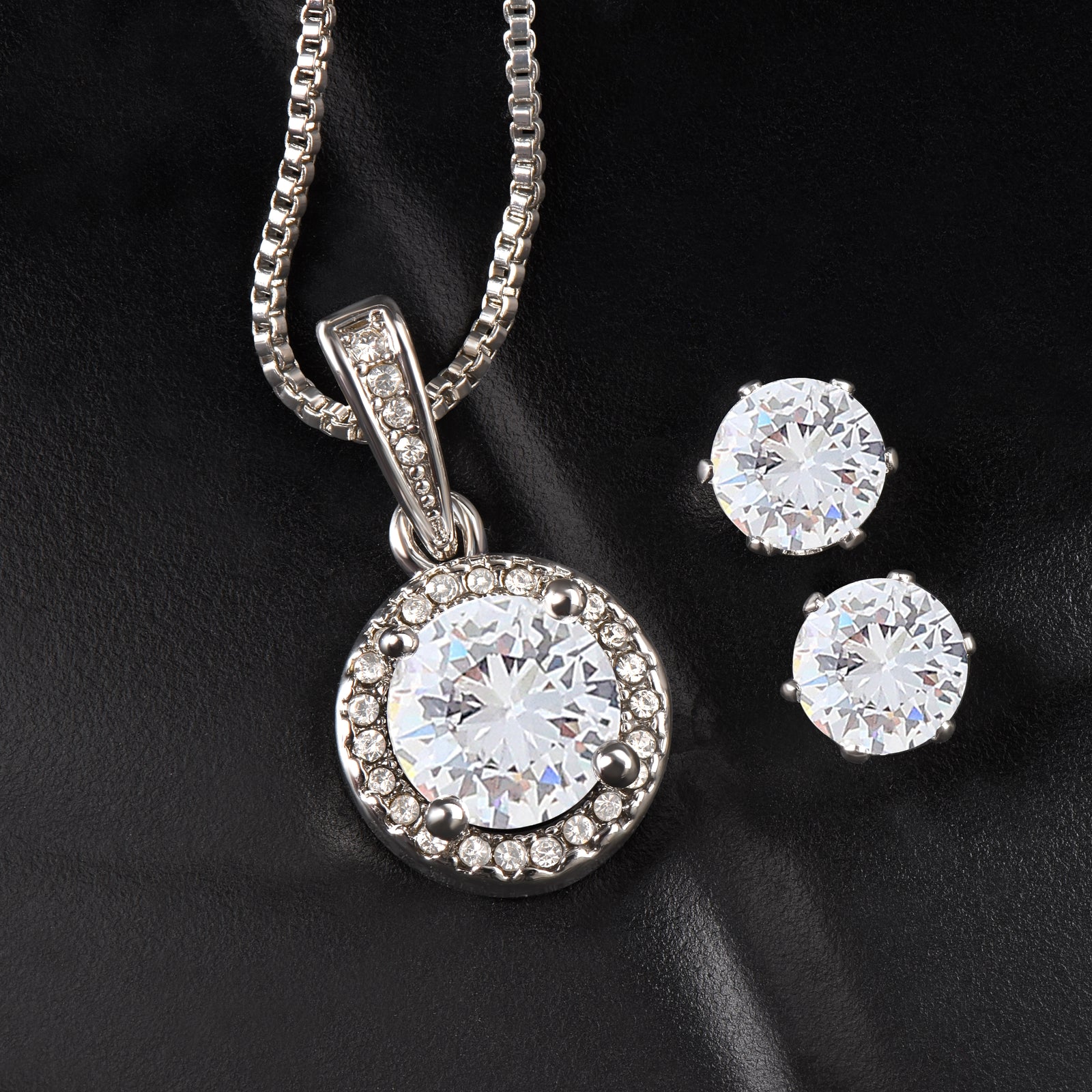 Silver-tone necklace with round cubic zirconia pendant surrounded by accent stones, displayed with matching round stud earrings on black background