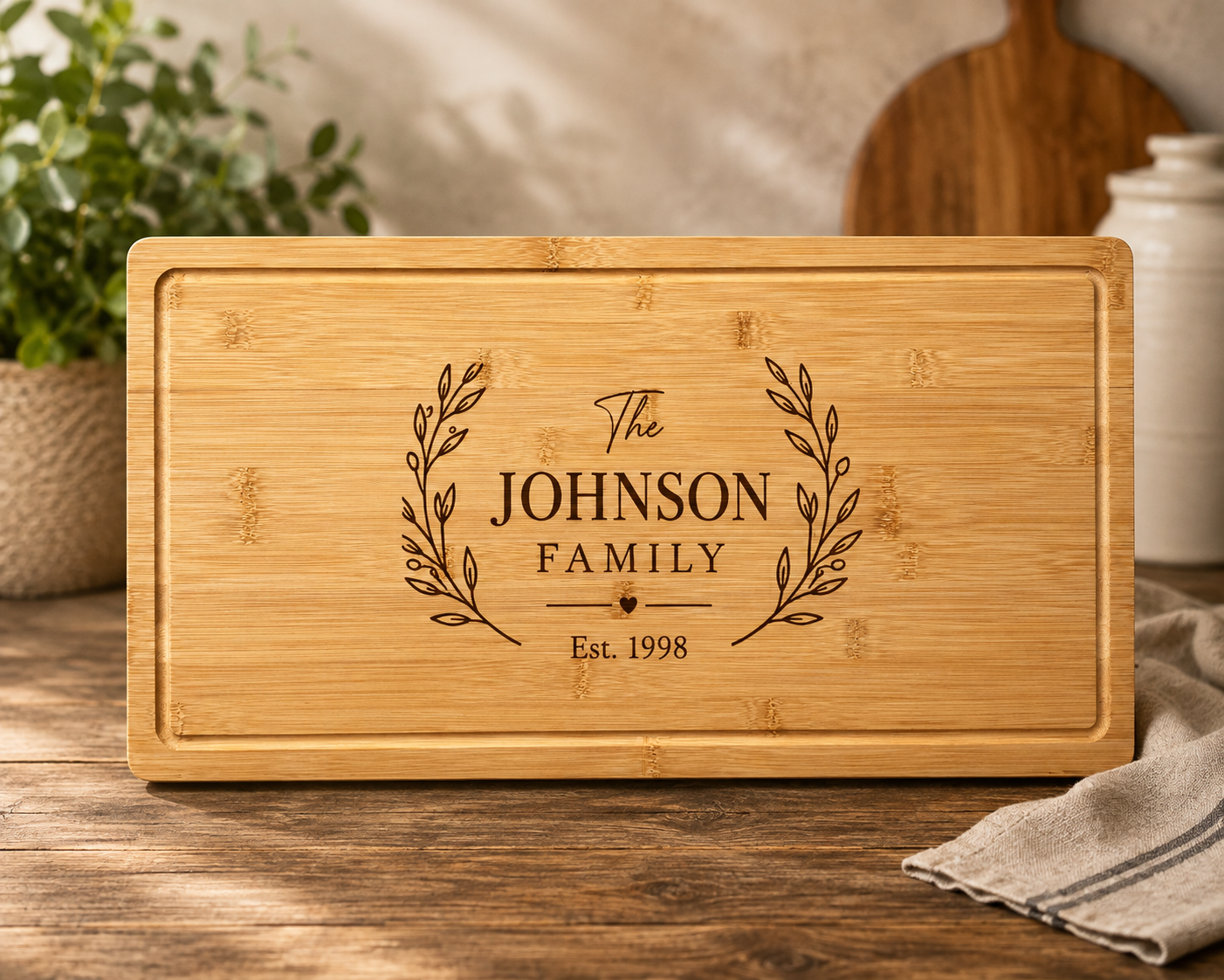 A rectangular bamboo cutting board with rounded corners, featuring a personalized engraving that reads 'The JOHNSON FAMILY Est. 1998' with leafy branches on either side.
