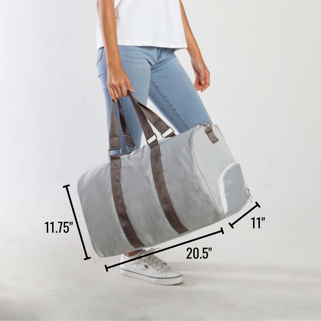 Light grey duffle bag with taupe handles and interior shoe compartment, displayed with dimensions 20.5" x 11.75" x 11" marked on the sides, held by woman in white tee and light jeans.