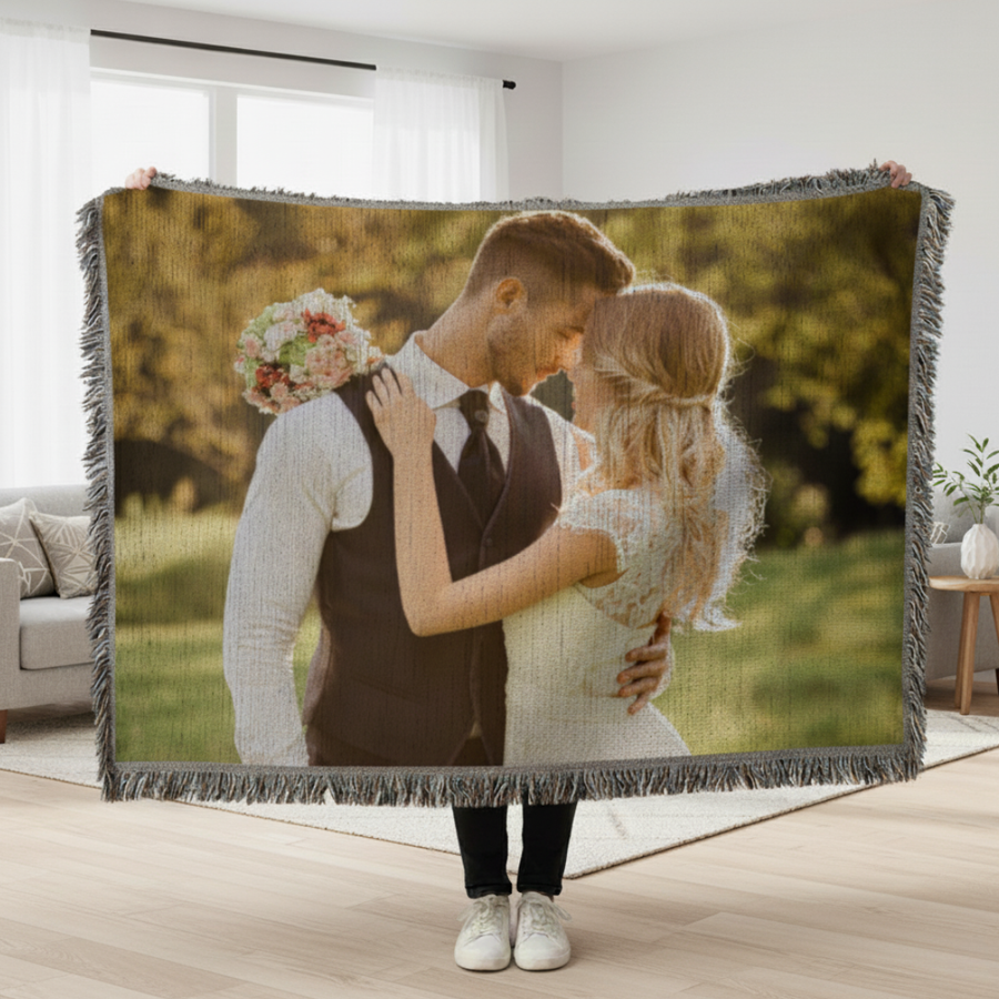Woven photo blanket with fringed edges displaying a bride and groom couple's portrait in an outdoor garden setting, held up by person standing indoors.