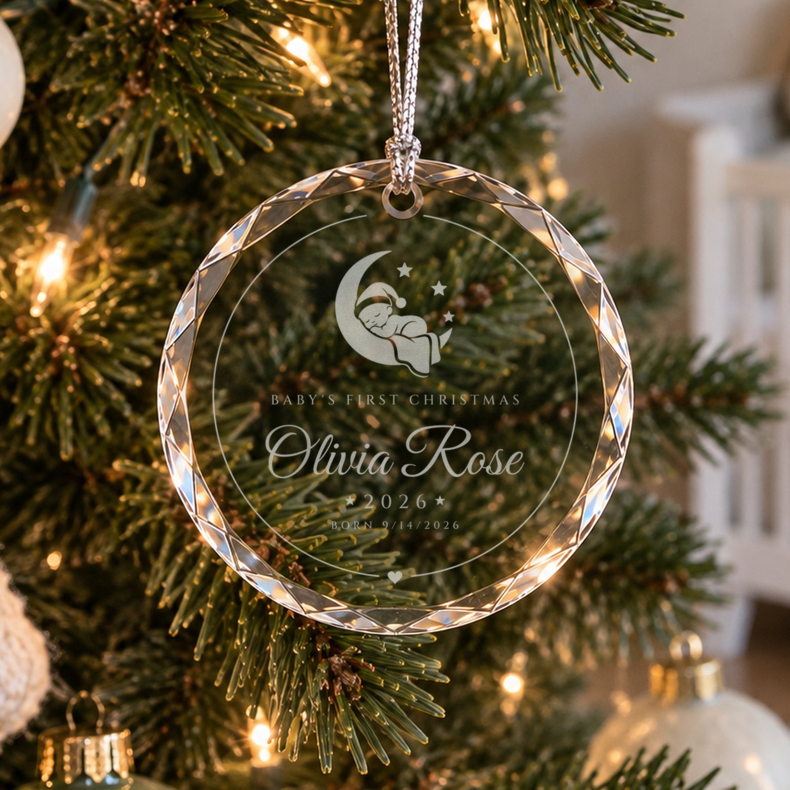 Personalized baby's first Christmas ornament in faceted glass on a soft white tree near a crib, engraved with a moon baby, Olivia Rose, 2026
