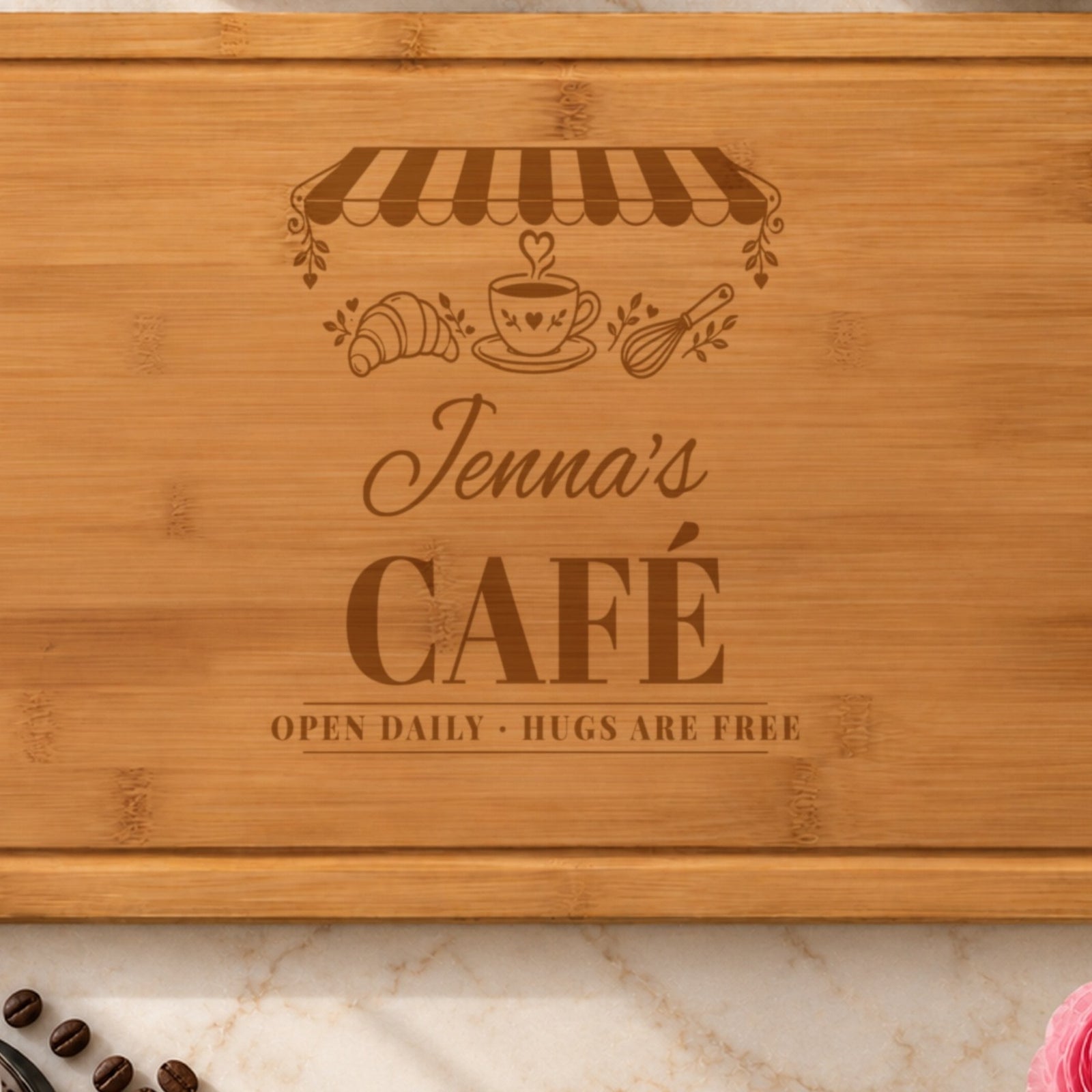 Close-up of the laser engraving on the cafe cutting board: the striped awning, heart-steam coffee cup, Jenna's in script and CAFÉ