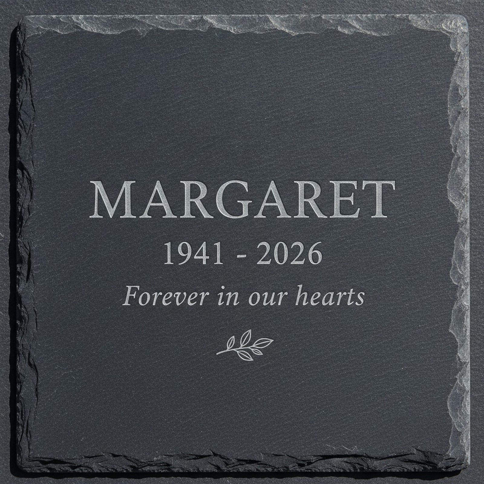 Close view of the recessed laser engraving on a natural slate memorial garden stone, the sample name Margaret cut pale into the dark stone above the years