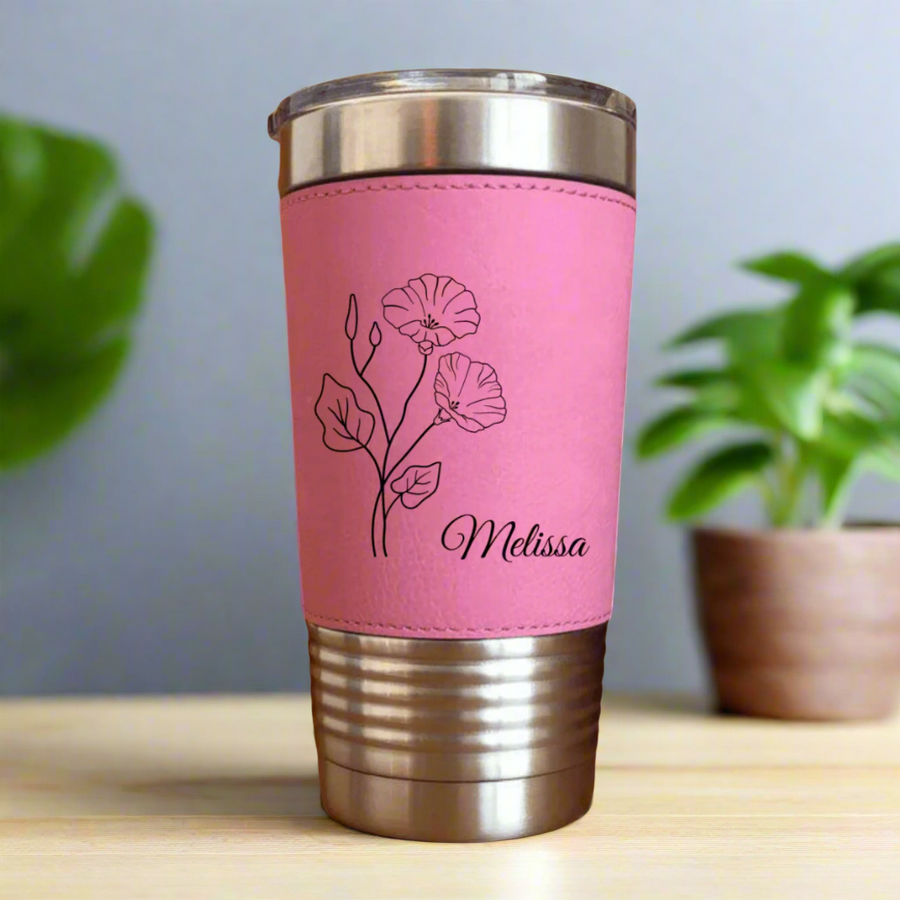 Pink tumbler with stainless steel top and bottom, wrapped pink faux leather band engraved with sample name "Melissa" and a line-drawn carnation flower design