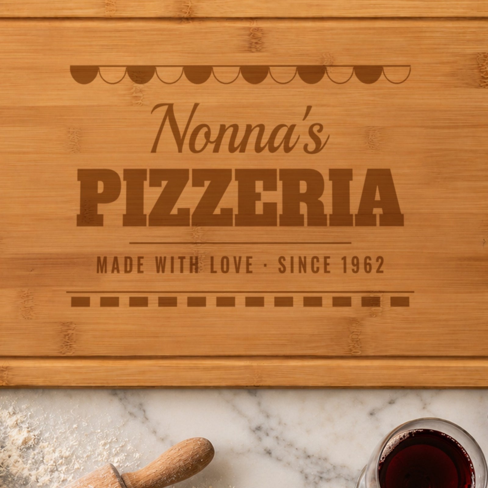 Close-up of the laser engraving on the pizza board: the striped awning, Nonna's in script and PIZZERIA burned into the bamboo grain