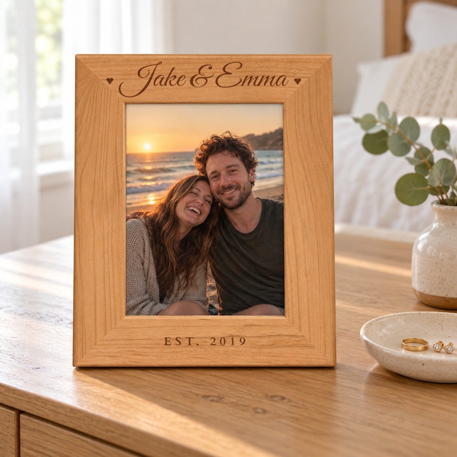 Our Names personalized picture frame in red alder wood engraved Jake & Emma with hearts and EST. 2019, holding a beach photo on a bedroom dresser