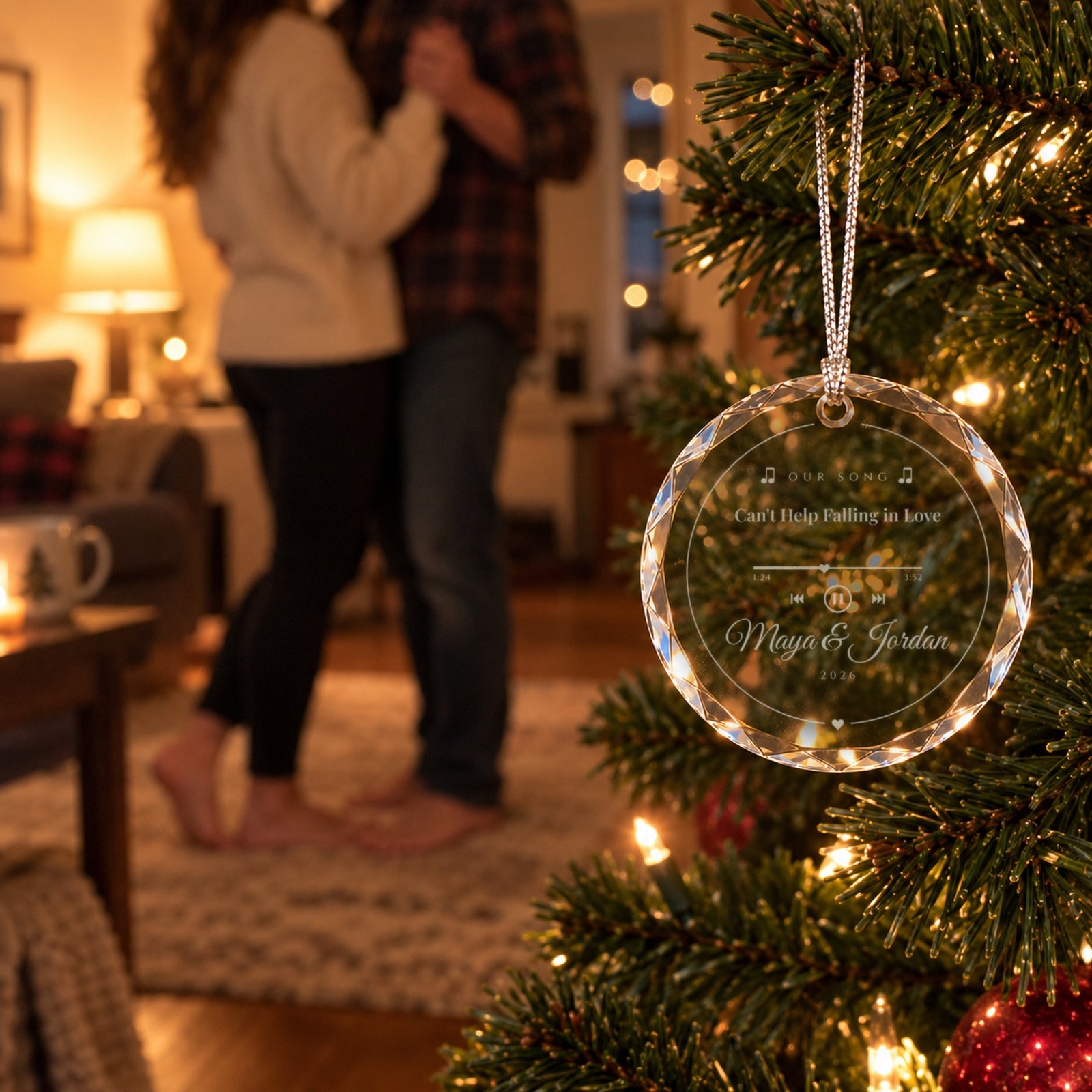 Couple slow dancing in the living room behind the engraved Our Song Christmas ornament on the tree, reading Can't Help Falling in Love