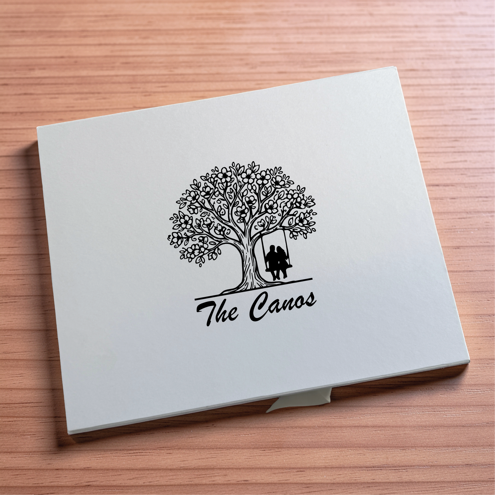 Gift box lid printed with a tree of life and a couple on a swing above the family name written in script.