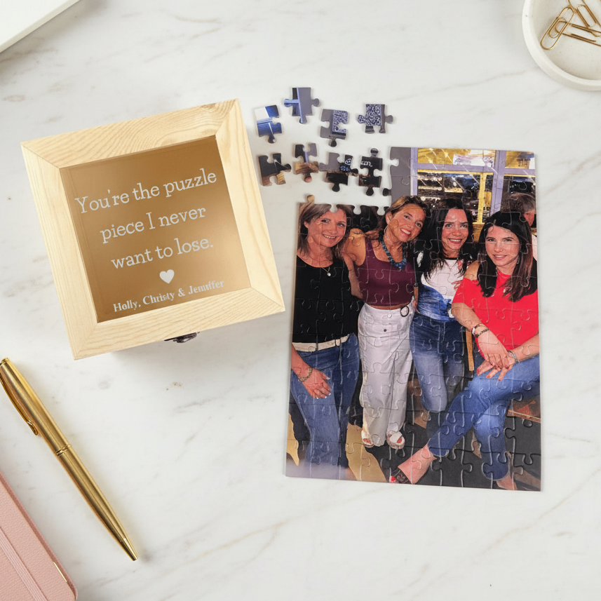 Wooden gift box with engraved message and photo puzzle showing four women, with scattered puzzle pieces displayed on marble surface