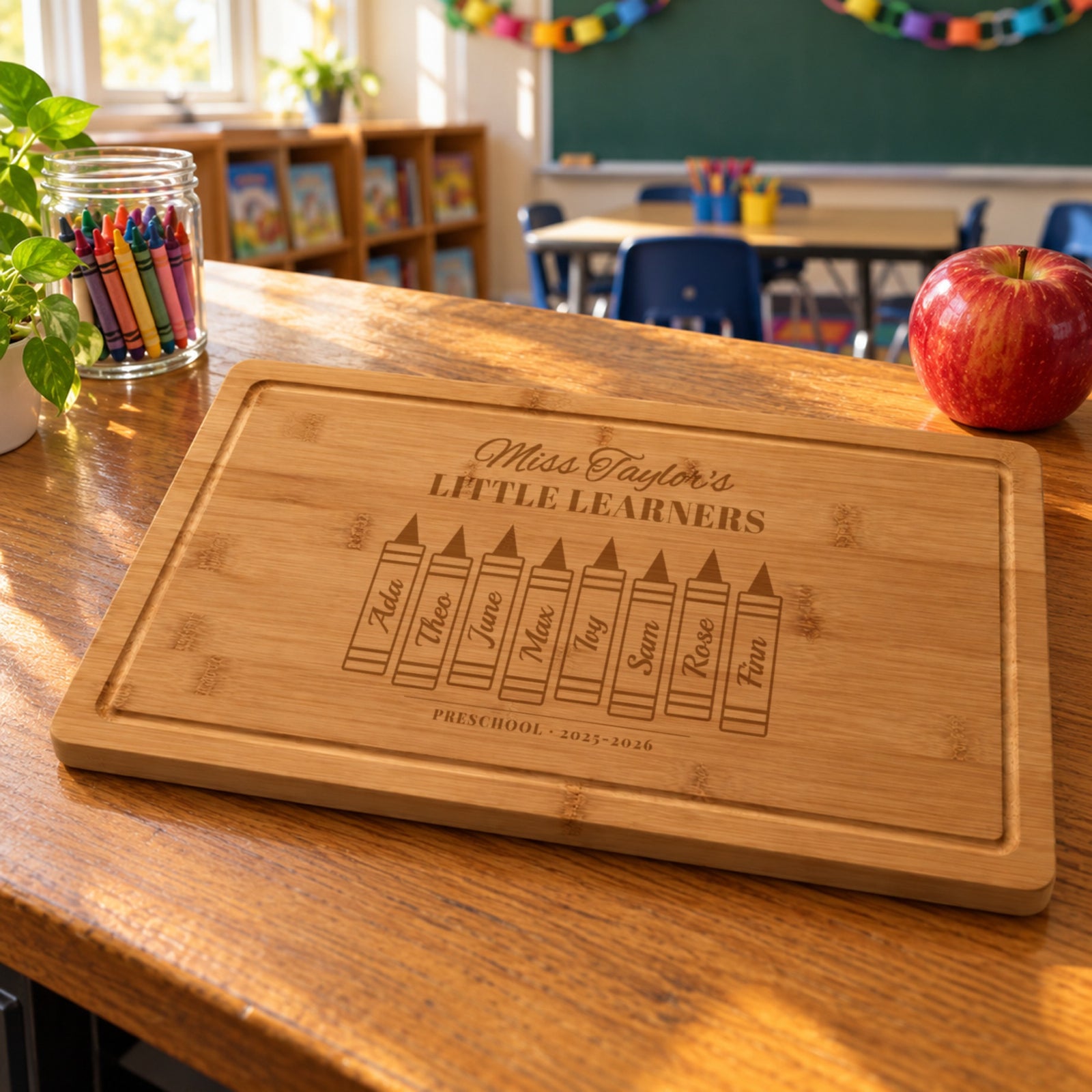 Class gift for a preschool teacher: bamboo board engraved Miss Taylor's LITTLE LEARNERS with eight student names on big crayons in a classroom
