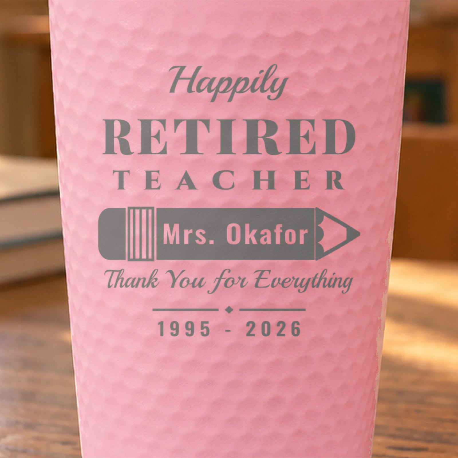 Close-up of the laser engraving on a pink dimpled tumbler: Happily Retired Teacher, Mrs. Okafor on a pencil and Thank You for Everything
