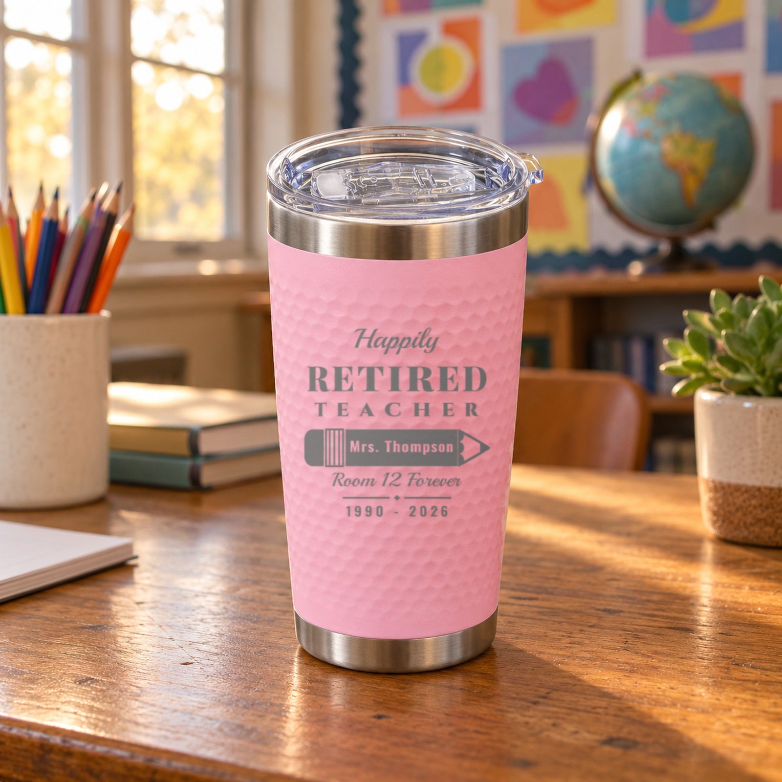 Pink teacher retirement tumbler engraved for Mrs. Thompson, Room 12 Forever, 1990 to 2026, on a classroom desk beside colored pencils