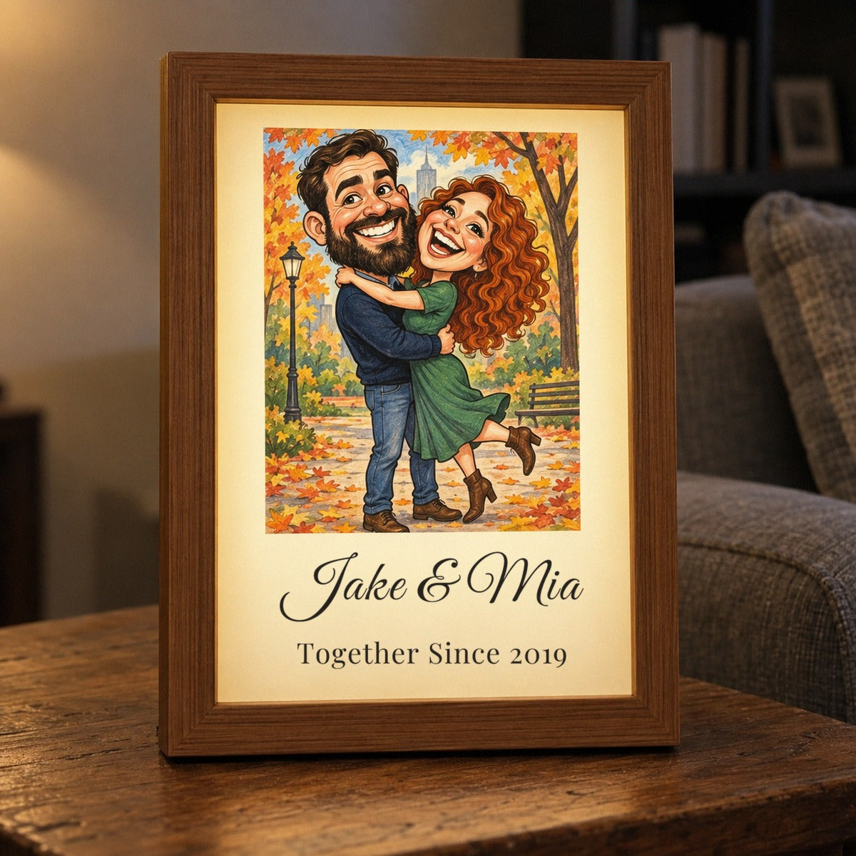 Custom caricature picture frame for a girlfriend lit up on a side table, a couple hugging in an autumn park drawn as a caricature, Jake &amp; Mia below