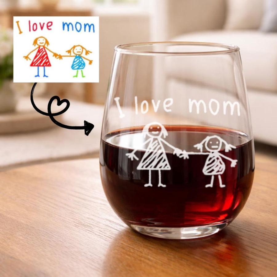 Stemless wine glass filled with red wine, laser-engraved with "i love mom" text and stick-figure drawings of two children, shown alongside reference artwork sample in upper left corner