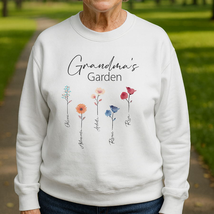 White crewneck sweatshirt with printed text "Grandma's Garden" and five watercolor flowers, each labeled with sample names Olivia, Aiden, Stella, Rosie, and Rae