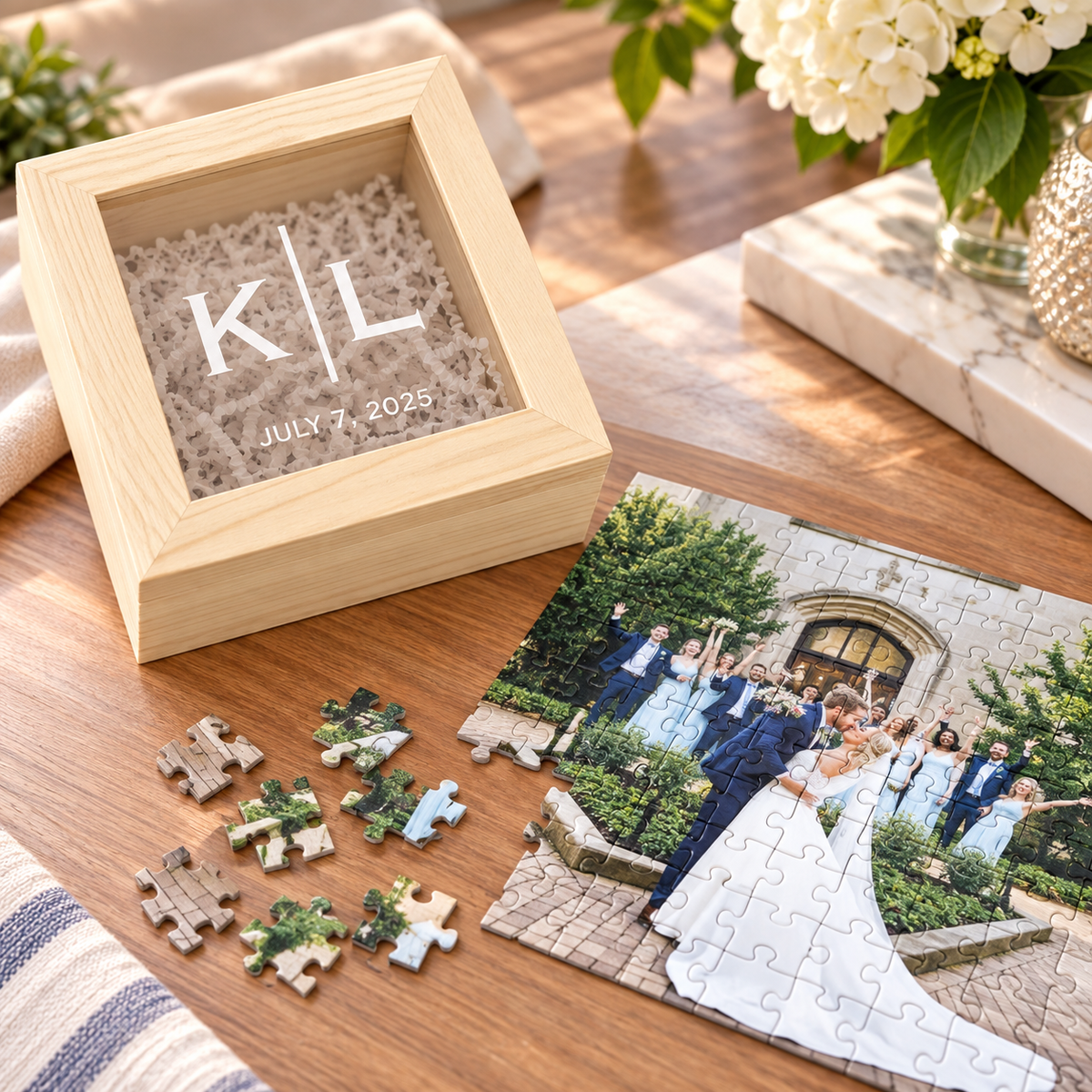 Light wood gift box with a glass window lid personalized with initials and a date, beside an assembled wedding photo puzzle and loose puzzle pieces on a wood table