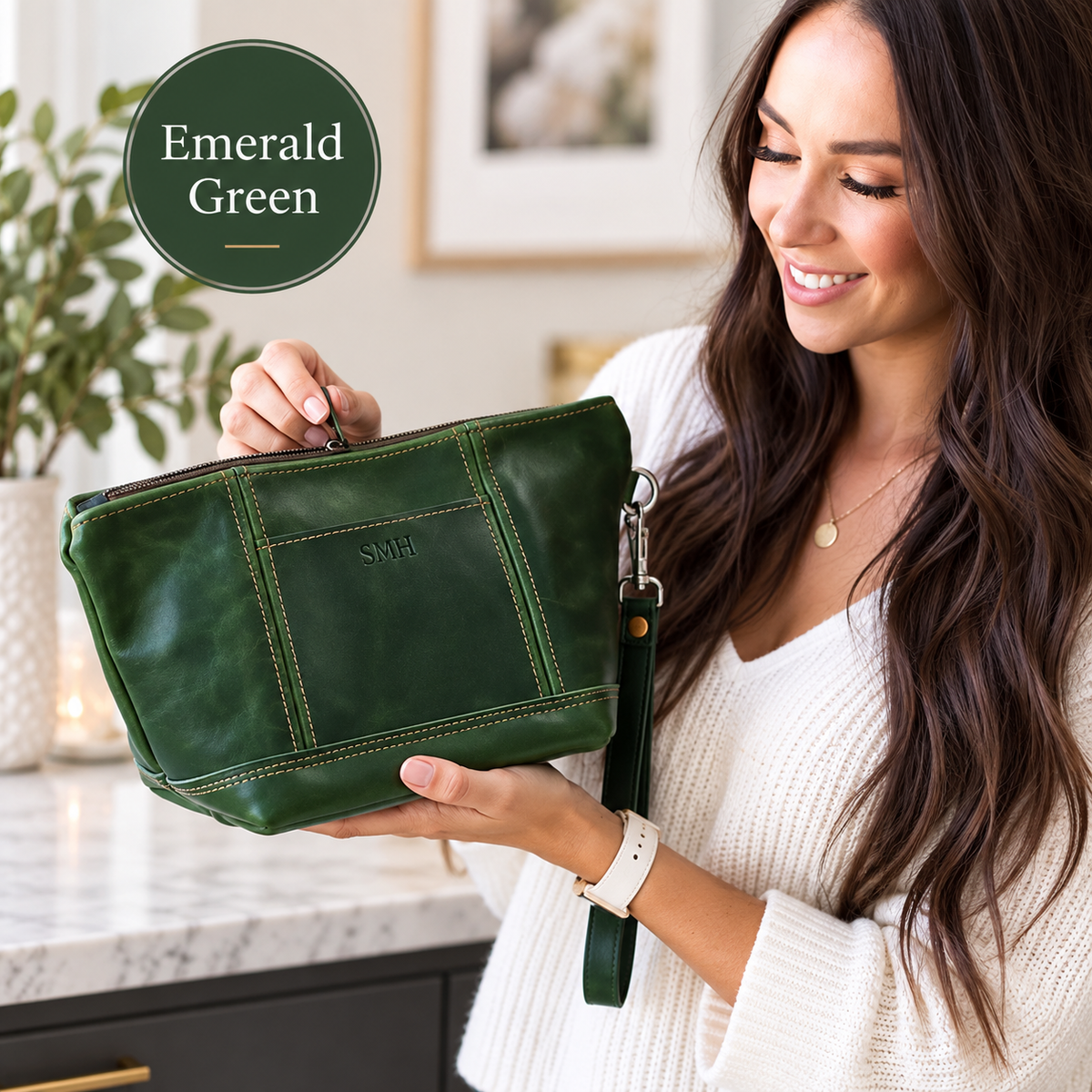 Emerald green leather toiletry bag with sample monogram "SW", displayed in hands with color swatch label and zipper pull visible.