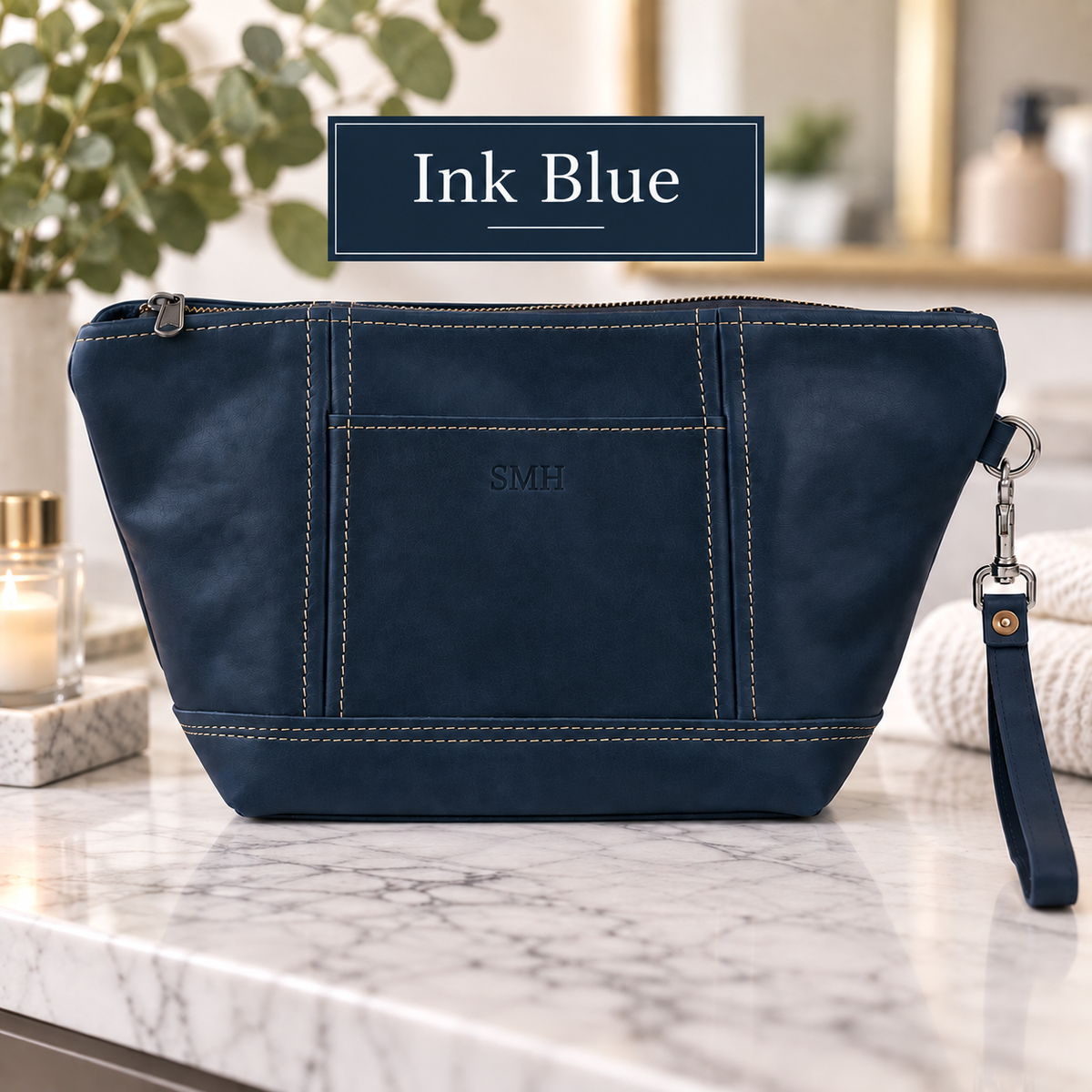 Ink blue leather toiletry bag with sample monogram "SMH" on front panel, contrast stitching, and detachable wrist strap