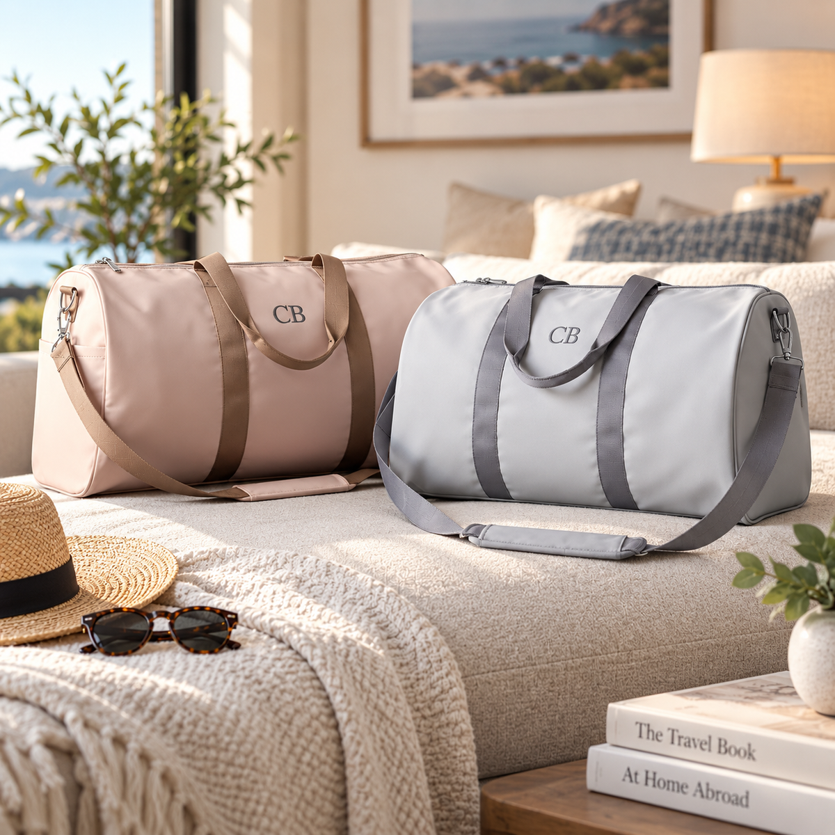 Blush and light grey personalized duffle bags side by side on a sofa, each embroidered with the initials 'CB' on the front panel.