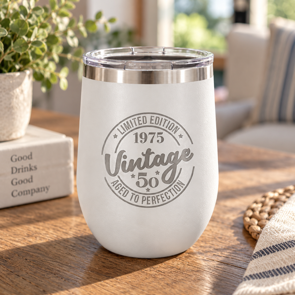White stemless wine tumbler laser engraved with a 'Vintage 1975, Limited Edition, Aged to Perfection' 50th birthday design, on a wood table.