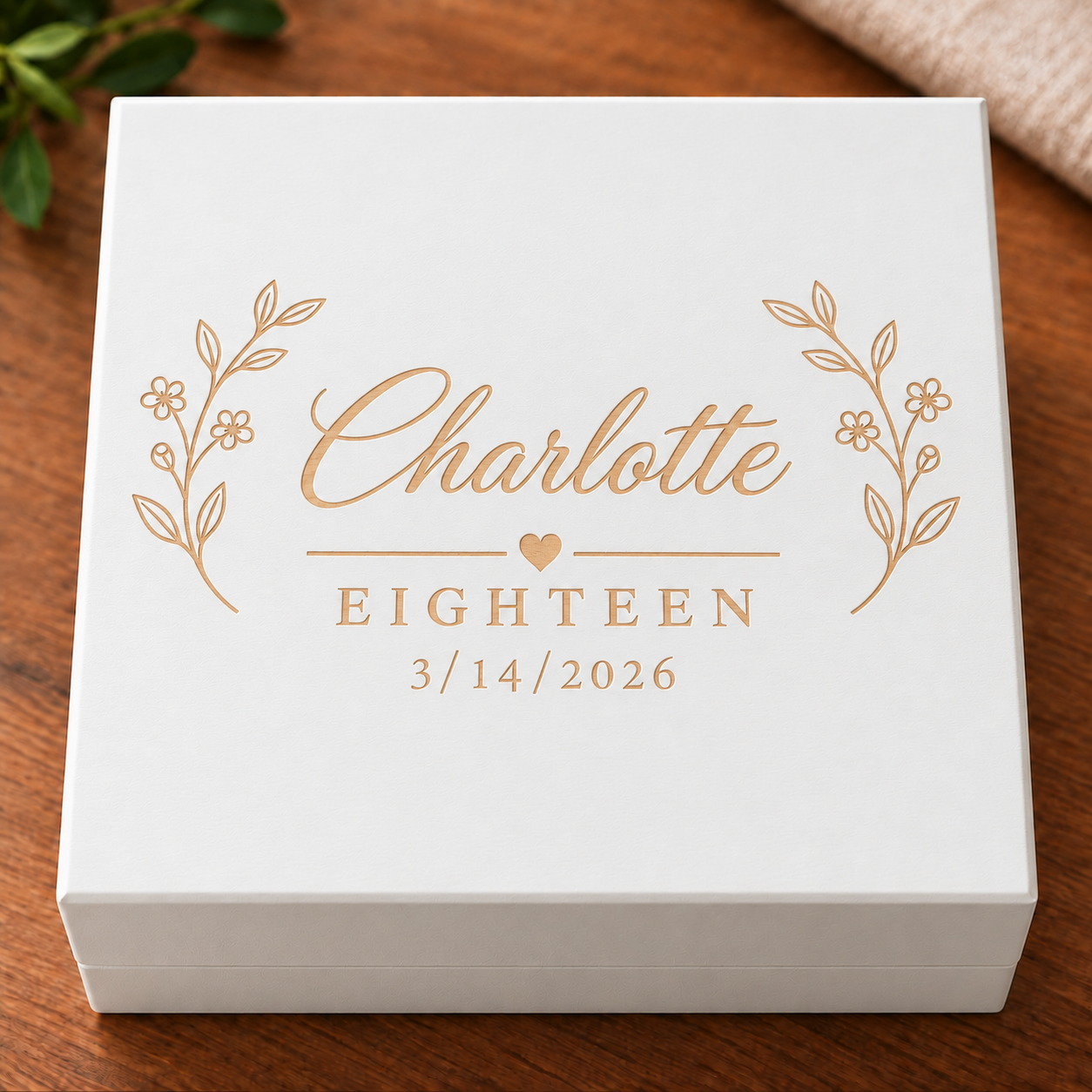 White keepsake box with rose gold foil engraving showing sample name "Charlotte", age "EIGHTEEN", and date "3/14/2026" with decorative leaf design.