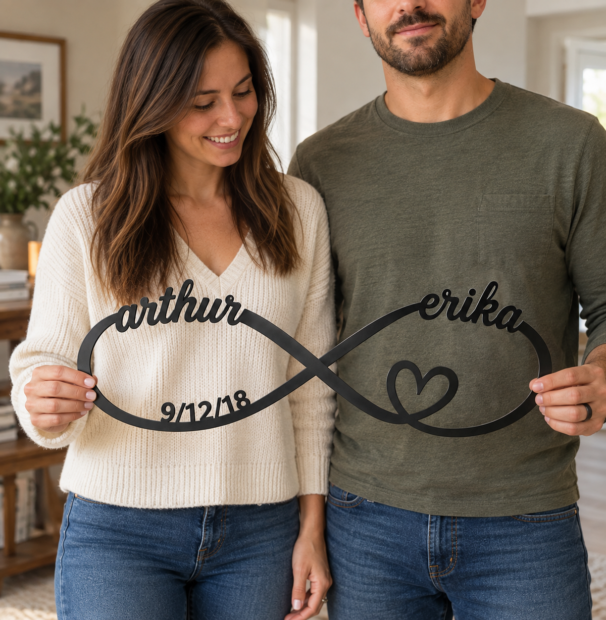 Couple holding a personalized metal infinity sign engraved with their names and anniversary date, standing together indoors