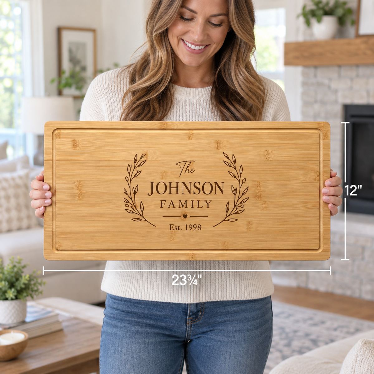 Personalized wooden charcuterie board with "The JOHNSON FAMILY" engraving, decorative laurel wreaths, and "Est. 1998" text, showing 23½" width and 12" height dimensions