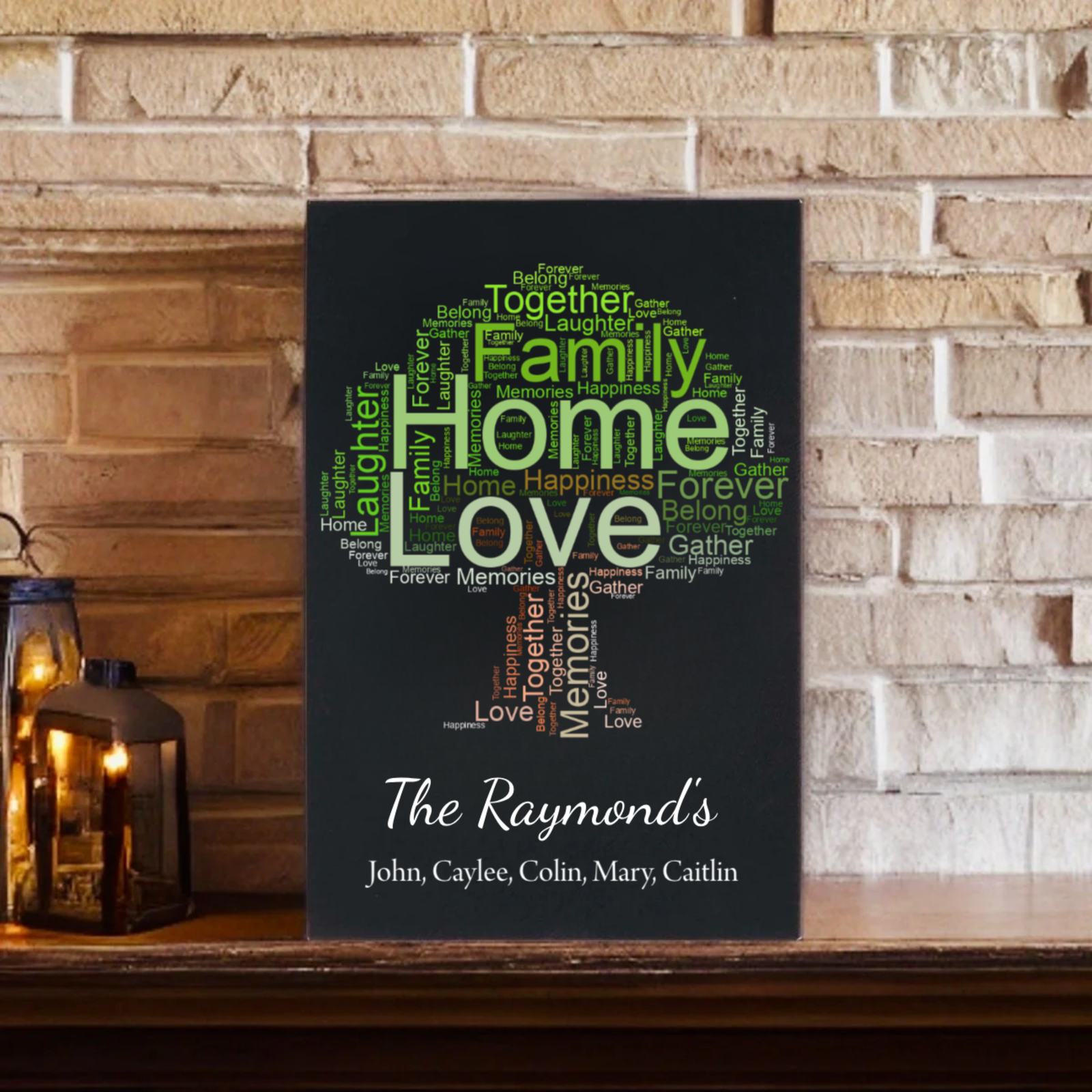 Black canvas word art sign featuring "Family," "Home," and "Love" in green and white text, personalized with sample family name "The Raymond's" and member names John, Caylee, Colin, Mary, Caitlin displayed on brick wall shelf with lantern