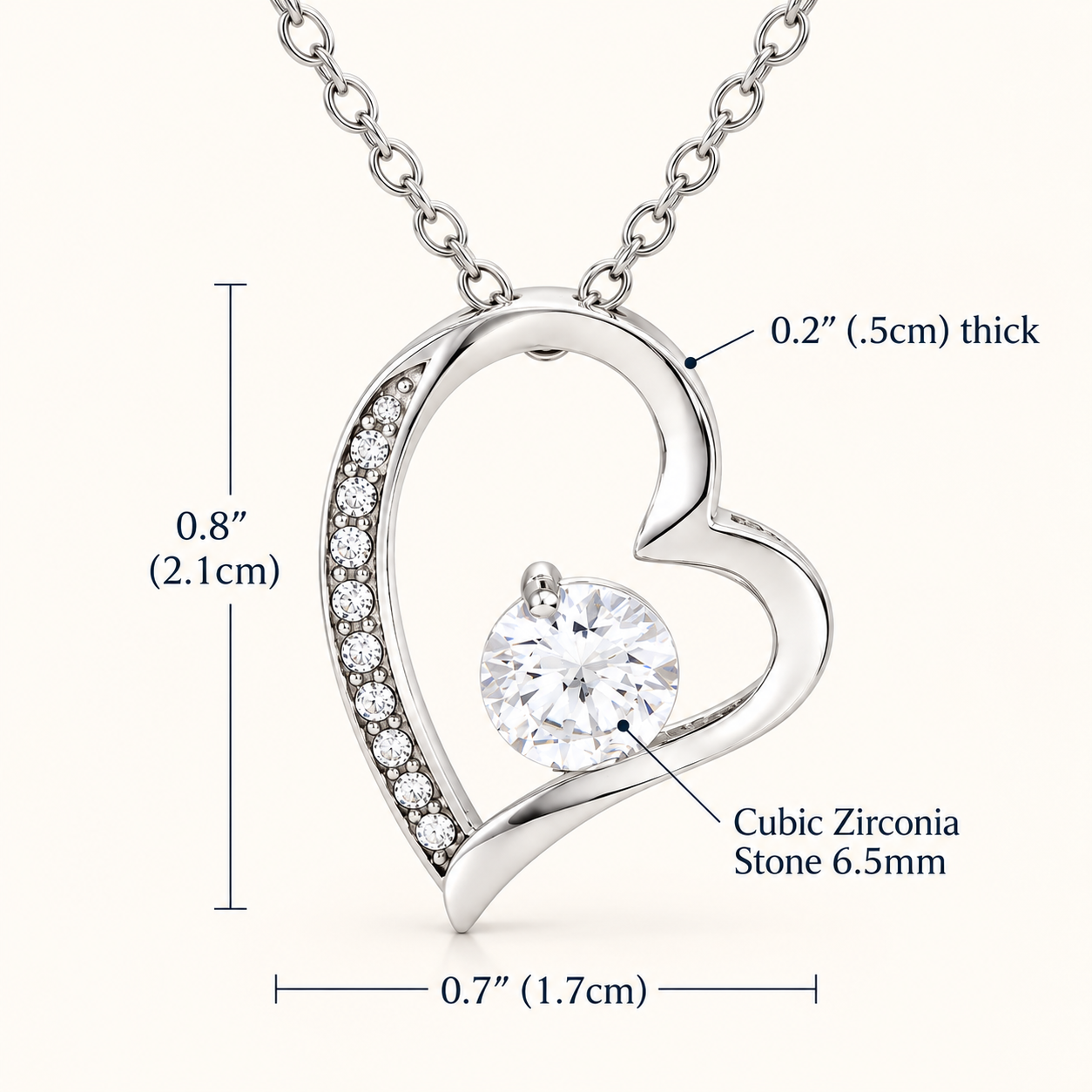 Silver heart-shaped pendant necklace with a clear round cubic zirconia stone and a row of small pavé stones on the left curve, shown on a light beige background with measurement callouts for height, width, and pendant thickness.