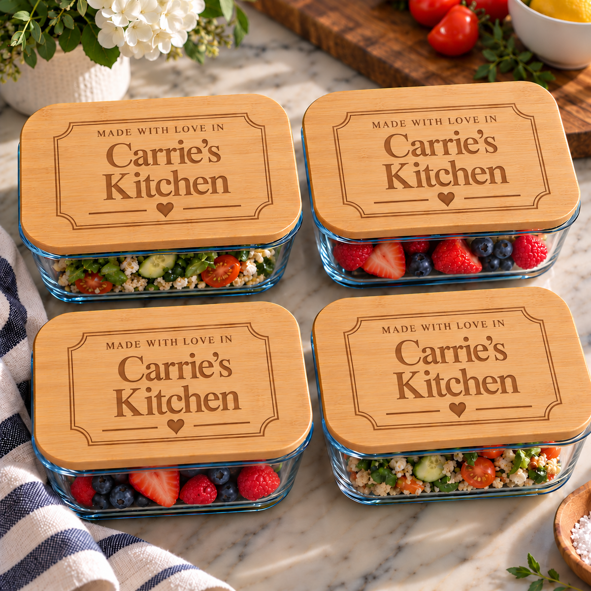 Four clear glass meal prep containers with rectangular lids, each topped with a natural wood lid engraved with the text 'MADE WITH LOVE IN Carrie's Kitchen