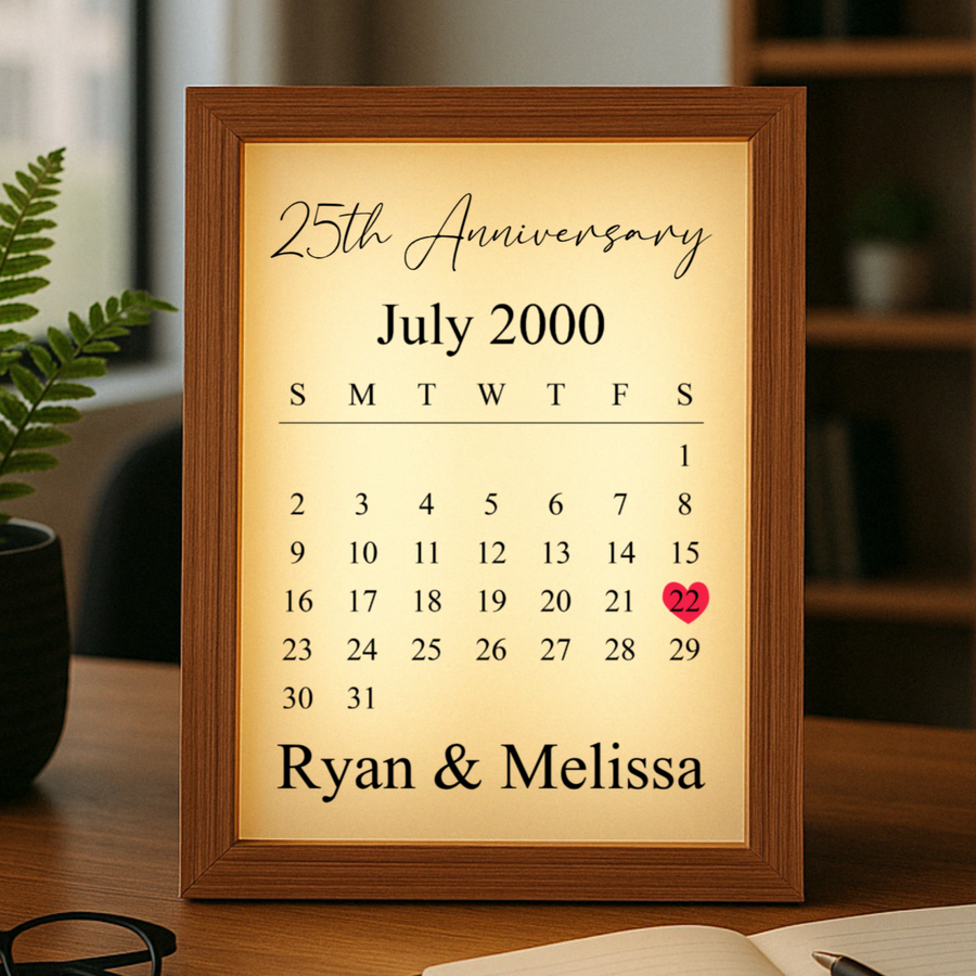 Framed calendar light box with wood border displaying "25th Anniversary" and July 2000 calendar with sample names "Ryan & Melissa" and red heart on the 22nd date.