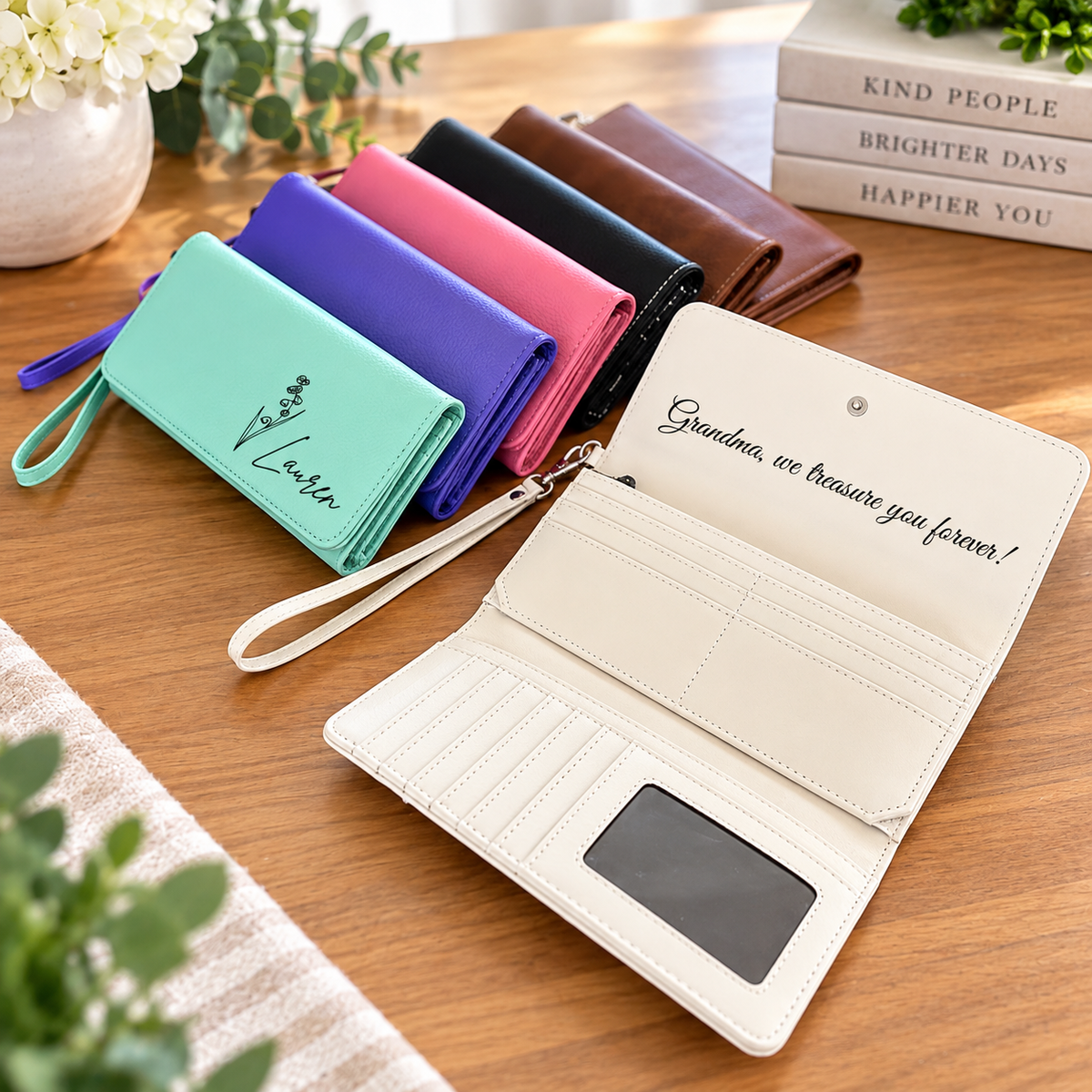 A set of faux leather wallet purses in various colors (mint green, light blue, pink, purple, black, brown, and cream) arranged on a wooden table. One cream wallet is shown open, displaying its interior card slots, a black ID window, and embroidered text 'Grandma, we treasure you forever!'.