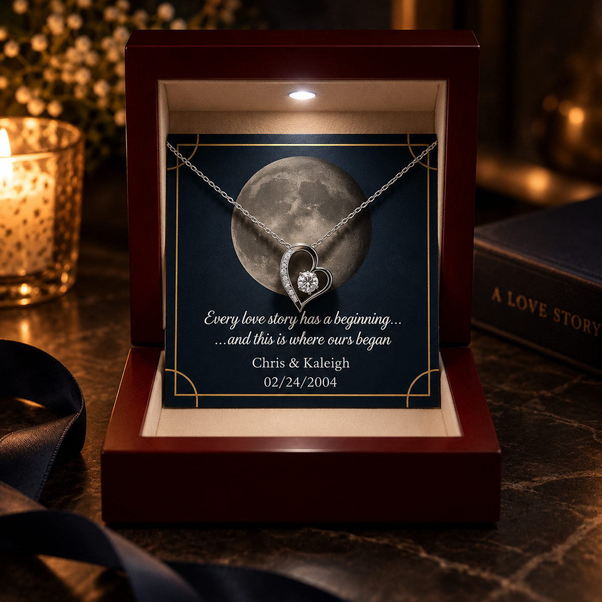 A personalized keepsake necklace displayed inside an open dark wood box with a built-in light. The necklace has a silver-toned heart-shaped pendant with a small clear gemstone.