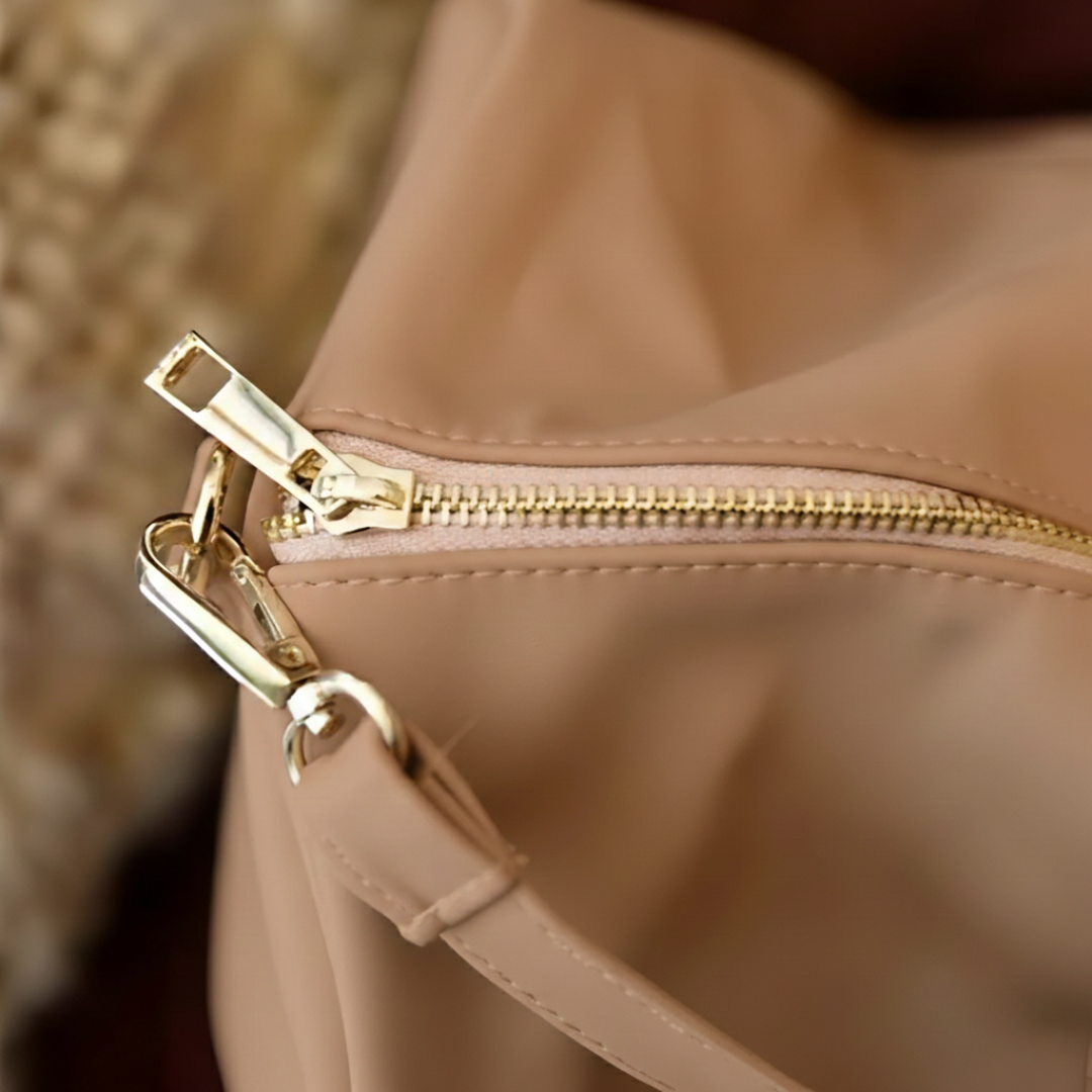 Close-up of tan vegan leather weekender bag showing gold-toned zipper pull and dual carry handles with stitched detailing.