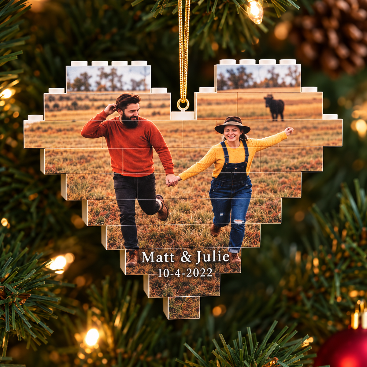 A heart-shaped Christmas ornament made of stacked photo tiles showing a couple running in a field, hanging on a Christmas tree with warm lights. Personalized text at the bottom reads 'Matt &amp; Julie 10-4-2022'.
