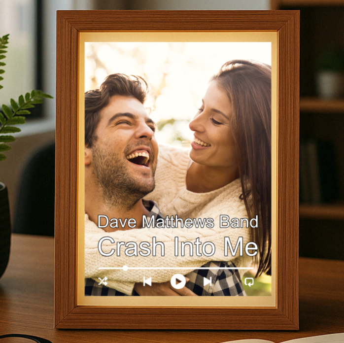 Wooden frame with warm LED light displaying a photo of a smiling couple, overlaid with sample text "Dave Matthews Band" and "Crash Into Me" with music player controls