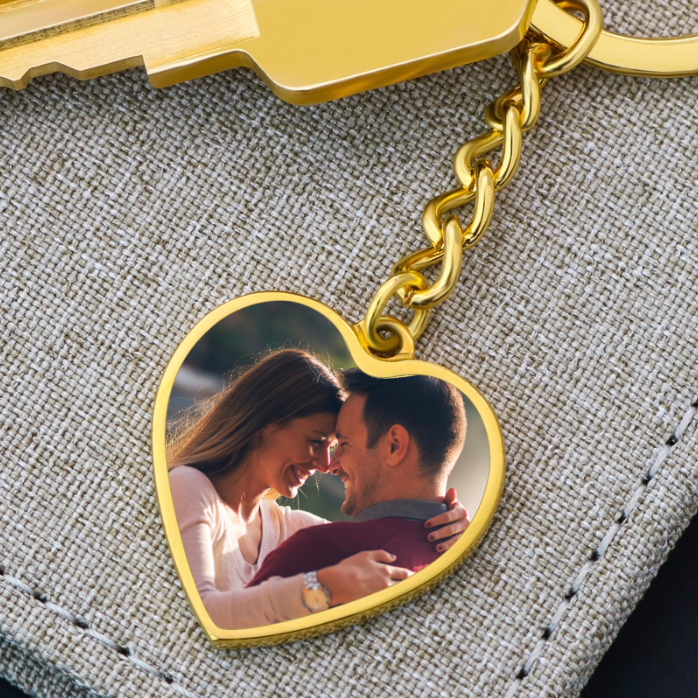 Heart-shaped gold photo keychain with chain attachment, displaying sample image of couple, resting on gray textured fabric
