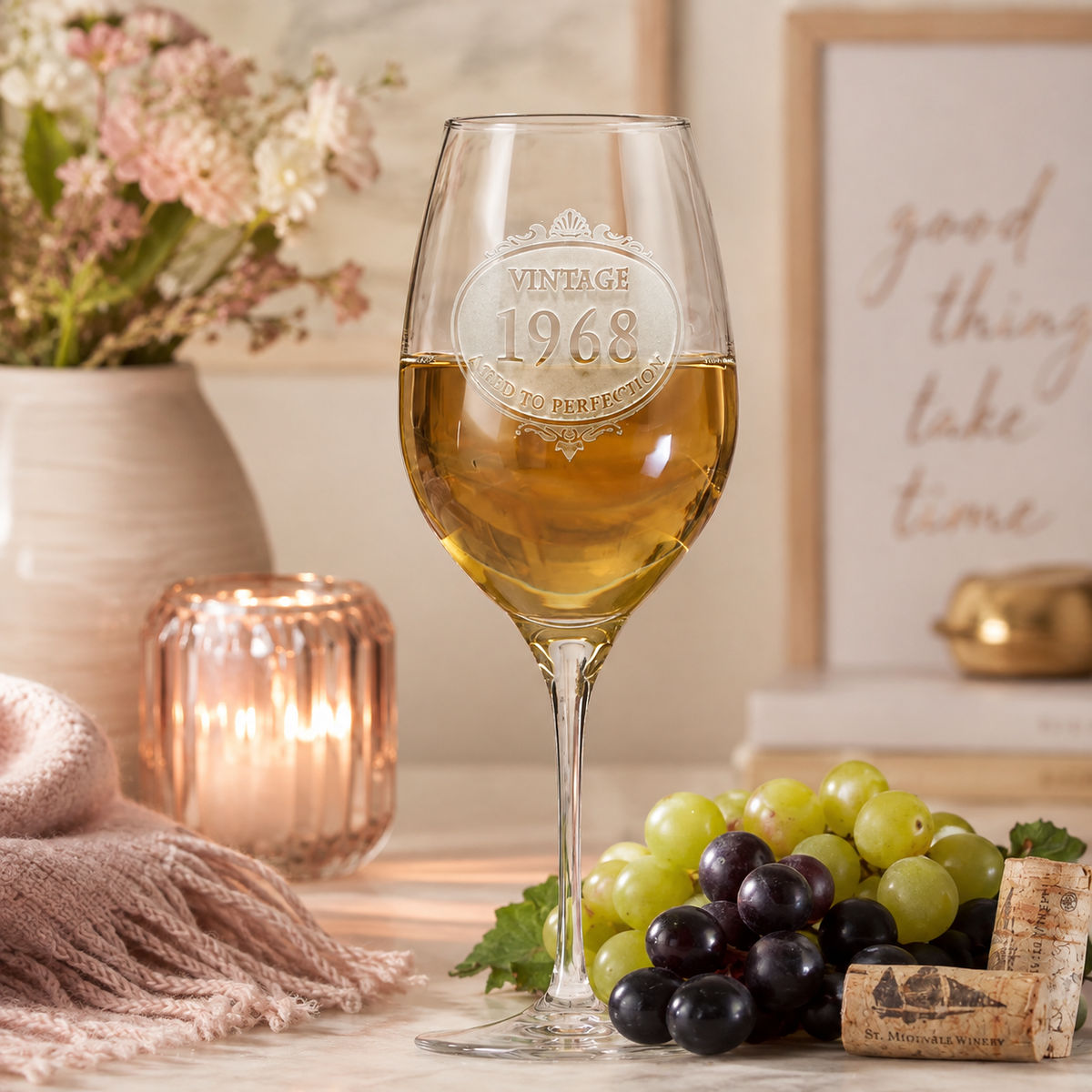 Engraved wine glass with sample vintage 1968 birthday design, filled with white wine, styled with flowers, grapes, and candle