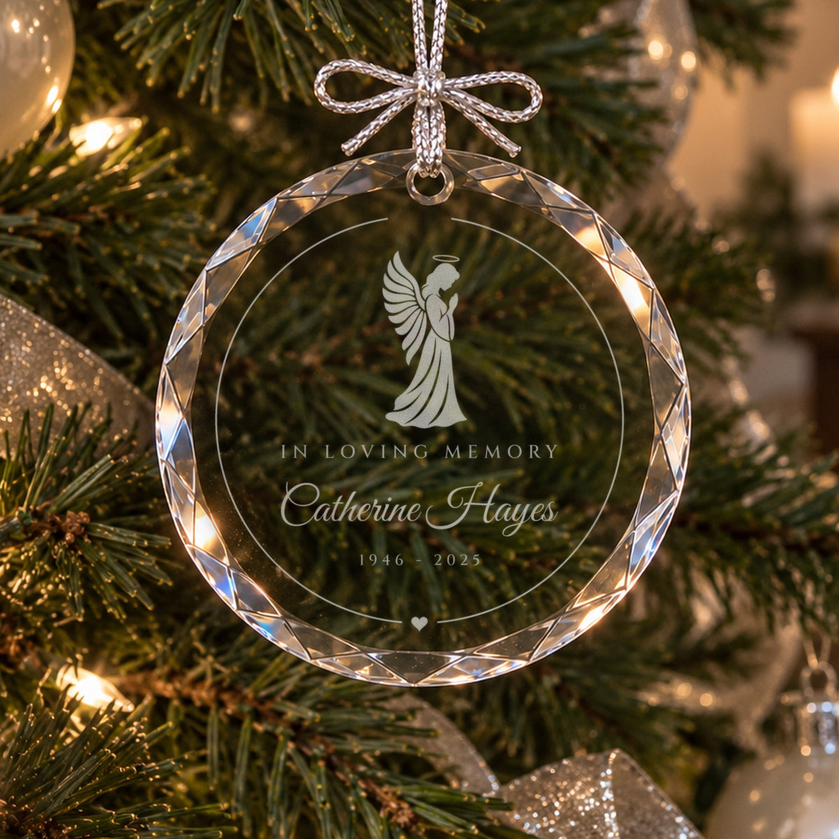 Personalized angel memorial ornament in faceted glass on a lit green Christmas tree with silver ribbon, engraved In Loving Memory, Catherine Hayes, 1946 to 2025